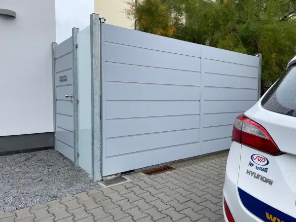 Exkluzivní hliníková dvoukřídlá brána s podzemními pohony, brankou a skleněným plotovým dílcem.