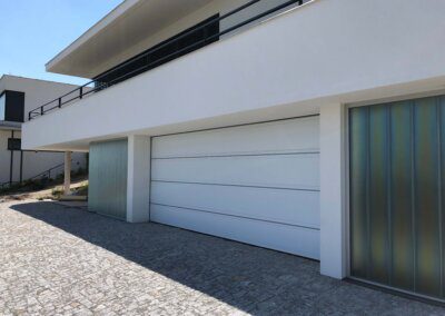 Sekční bílá garážová vrata Hörmann LPU, drážka "T" s ozdobným vodorovným nerezovým pruhem, hladký povrch SilkGrain na moderní vile. Jednoduché a elegantní řešení vrat do garáže.